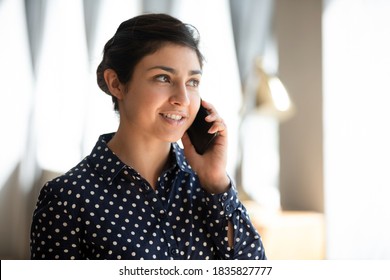 Head Shot Portrait 30s Indian Business Woman Standing Indoor Talk On Smart Phone With Company Client, Looking Into Distance Feels Confident Arrange Meeting, Ordering Taxi Services By Phonecall Concept