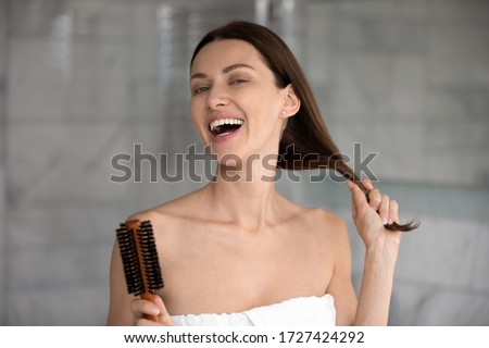 Head shot portrait 35s cheerful woman after take a bath holds hairbrush tidy her strong healthy hair, morning beauty routine lifestyle, treatment for perfect hair growth advertising, haircare concept