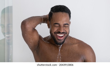 Head shot portrait African man take shower, enjoy morning bath standing under running water, do daily routine, smiling rinse off shampoo. Healthcare, hygiene, bodycare, male beauty cosmetics concept