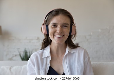 Head Shot Portrait Attractive Freckled Woman In Headphones Staring At Camera, Make Distance Conversation Via Video Conference App Call At Home. Seeker Pass Job Interview, Streaming Event, Tech Concept