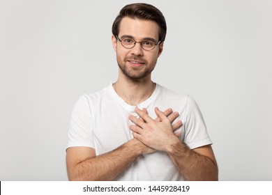 Head shot portrait attractive guy in white t-shirt look at camera feel grateful, man holds hands on chest heart symbol of love, moment of sincere gratitude and thankfulness isolated on gray background - Shutterstock ID 1445928419