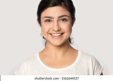 Head shot portrait close up beautiful Indian girl with beaming healthy smile and perfect skin isolated on grey background, pretty attractive young woman looking at camera, natural beauty makeup