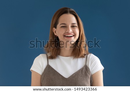 Head shot portrait close up happy young woman with wide healthy smile looking at camera, beautiful girl laughing at funny joke, having fun, feeling positive, isolated on blue background