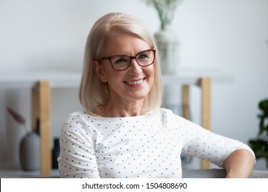 Head Shot Portrait Close Up Smiling Mature Woman Wearing Glasses Looking In Distance, Dreaming, Thinking Of Future, Older Female With Healthy Smile Sitting On Couch At Home, Posing For Photo