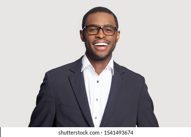 Head shot portrait close up smiling successful African American businessman looking at camera, laughing, excited man wearing formal suit and glasses isolated on grey studio background