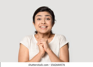 Head shot portrait close up smiling Indian girl joining hands with excitement, surprised beautiful young woman looking at camera, excited by good news, isolated on grey studio background