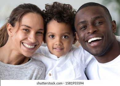 Head shot portrait close up smiling African American mother, father and son with healthy white smiles, happy family posing for photo, looking at camera, cute little child embracing parents