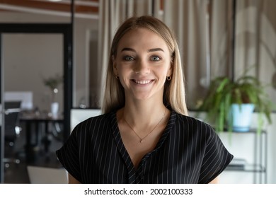 Head shot portrait close up of smiling young businesswoman intern looking at camera, standing in modern office room, successful confident employee happy female posing for corporate profile picture