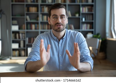 Head shot portrait confident businessman coach wearing glasses looking at camera and talking, mentor speaker holding online lesson, explaining, sitting at wooden work desk in modern cabinet - Shutterstock ID 1714666162