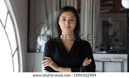 Head shot portrait confident Indian businesswoman hr manager standing in modern office with arms crossed, serious entrepreneur team leader mentor posing for corporate photo, looking at camera