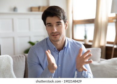 Head Shot Portrait Confident Young Man Speaking At Camera, Making Video Call To Friends Or Relatives, Sitting On Couch, Mentor Teacher Holding Online Lesson, Explaining, Blogger Recording Vlog