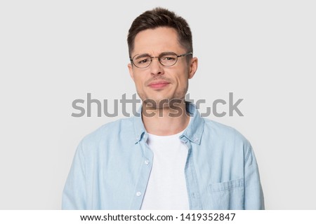 Head shot portrait dissatisfied man in eyeglasses frowning eyebrows having dissatisfied grumpy face expression posing over grey white studio background negative emotions irritated person concept image