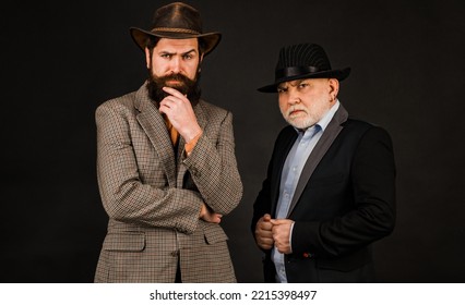 Head Shot Portrait Of Elderly Mature Dad And Grownup Son. Two Male Generations Family. Men In Hat On Dark Studio Background. Generations Family Young Old.