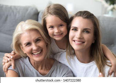 Head shot portrait granddaughter mother and grandmother sitting together on sofa at home looking at camera smiling feeling good and satisfied spend free time together. Happy mother day holiday concept - Powered by Shutterstock