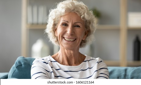 Head shot portrait grey-haired positive elderly woman 65 70 years resting on couch smiling looking at camera feels happy enjoy retired life, having wide toothy smile dentures dental services concept