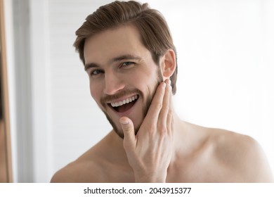 Head shot portrait handsome man look in mirror do skincare facial after bath or shower routine, enjoy smooth skin after applied face lotion, touch beard check trimming styling result. Hygiene concept