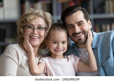 Head shot portrait of happy adorable little preschool 7s kid girl cuddling affectionate middle aged older granny and loving young father, posing for photo together at home, family relations concept. - Powered by Shutterstock