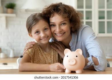 Head shot portrait of happy cute little daughter and mother with piggy bank, smiling mom and adorable girl child looking at camera, saving money for future, family insurance and investment concept