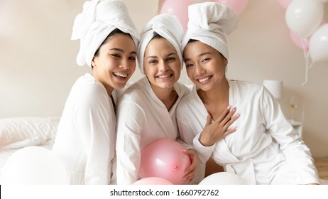 Head shot portrait happy diverse young women wearing bathrobes and towel on heads celebrating wedding or birthday in spa, sitting on bed together, looking at camera, having fun at hen party - Powered by Shutterstock