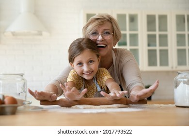 Head shot portrait happy mature grandmother in glasses with granddaughter rolling dough together, looking at camera, excited senior woman with adorable little girl cooking cookies in kitchen - Powered by Shutterstock