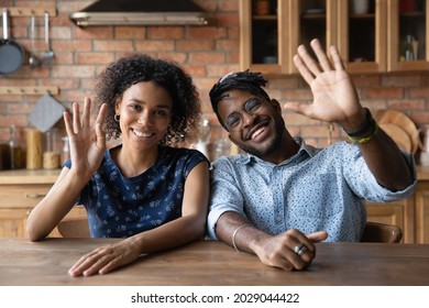 Head shot portrait of happy millennial Black mixed race husband and wife making video call from home, looking and speaking at webcam, waving hello, smiling at camera. Couple of bloggers, coaches