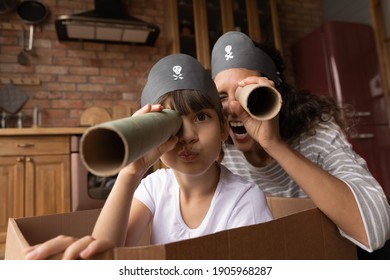Head shot portrait happy mother and little daughter playing pirates, looking at camera, excited mum and preschool gild child wearing handmade costumes, holding paper tubes as spyglass, having fun