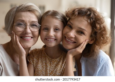 Head shot portrait happy three generations of women posing for family picture together, smiling mature grandmother and mother with adorable little girl looking at camera, warm family relationship