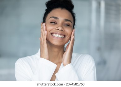 Head shot portrait of happy young african american woman in bathrobe looking at camera, touching face, feeling excited of fresh clean moisturized skin, doing professional domestic spa skincare routine - Powered by Shutterstock