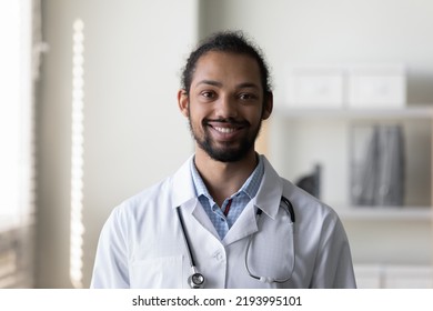 Head Shot Portrait Of Happy Young African American Doctor, Physician, Therapist General Practitioner In White Coat With Stethoscope Posing In Hospital Office, Looking At Camera, Smiling