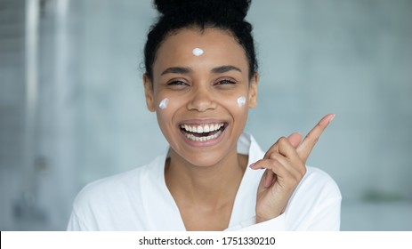 Head shot portrait laughing African American woman with moisturizing cream or mask on face pointing finger at copy space, smiling beautiful girl advertising skincare cosmetics, spa treatment - Powered by Shutterstock