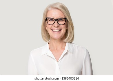 Head shot portrait laughing old businesswoman in glasses white blouse looks at camera feels happy pose isolated on grey studio background, experienced professional business coach teacher concept image