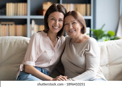 Head Shot Portrait Mature Woman With Grown Up Daughter Hugging, Holding Hands, Sitting On Cozy Couch At Home, Smiling Young Female With Older Mother Posing For Family Photo, Enjoying Leisure Time