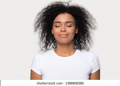 Head shot portrait mixed race attractive calm woman in white t-shirt isolated on grey background, closed eyes smile enjoy fresh air dreaming about future feels satisfied and tranquil conceptual image