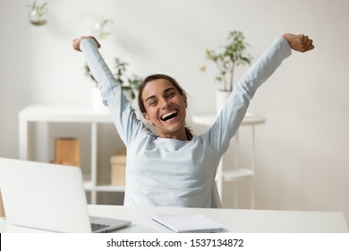Head shot portrait overjoyed smiling young mixed race lady rising hands, stretching back, relaxing after finishing project. Happy millennial woman employee celebrating working day finish at office.