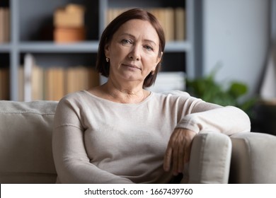 Head Shot Portrait Peaceful Tranquil Middle Aged Old Woman Resting On Cozy Sofa Alone At Home. Pleasant Happy Senior Mature 60s Grandmother Relaxing On Couch In Living Room, Posing For Photo.