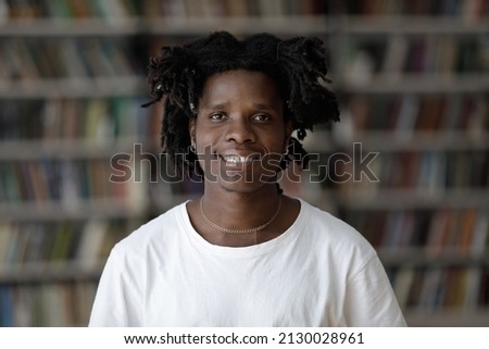 Head shot portrait of pleasant handsome happy African American male student with curly hairstyle posing in library. Profile photo of joyful millennial confident multiracial guy looking at camera.