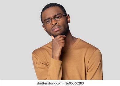 Head shot portrait sceptical African guy wearing mustard color jumper glasses looking at camera touch chin make decision looking concerned posing isolated on gray background, doubting person concept