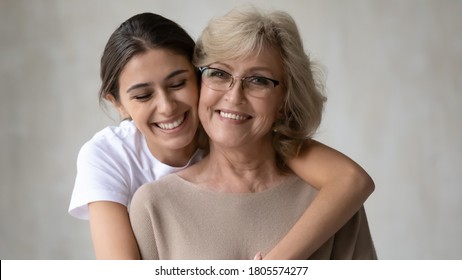 Head shot portrait of sincere smiling young arabic ethnicity woman cuddling happy middle aged 60s mother in glasses. Different generations mixed race family bonding, showing love looking at camera.