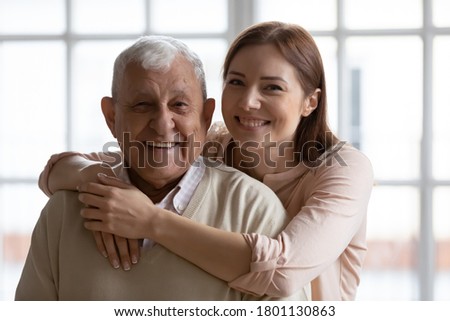 Head shot portrait of smiling affectionate loving grown up daughter cuddling devoted old senior father indoors. Caring young woman enjoying tender free weekend moment with retired daddy at home.
