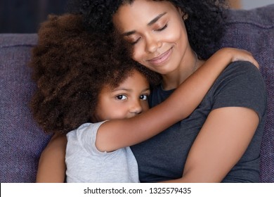 Head Shot Portrait Smiling African American Mother Embracing Little Daughter With Tenderness, Close Up, Warm Relationships Between Parent And Child, Looking At Camera, Sitting On Sofa At Home