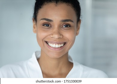 Head shot portrait smiling African American young woman with healthy perfect smooth skin looking at camera, attractive girl wearing bathrobe standing in bathroom, skincare and natural beauty concept