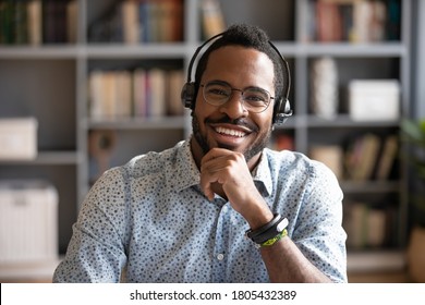 Head Shot Portrait Smiling African American Man Wearing Headphones And Glasses Looking At Camera, Posing For Photo In Modern Cabinet, Happy Satisfied Male Customer Service Operator In Headset