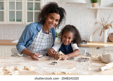 Head Shot Portrait Smiling African American Mother With Little Daughter Cooking Homemade Pastry Together, Happy Young Mom And Adorable 5s Girl Child Looking At Camera, Standing In Kitchen At Home