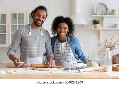 Head Shot Portrait Smiling African American Couple Cooking Homemade Cookies Or Pie Together, Standing In Kitchen, Looking At Camera, Happy Young Man Rolling Out Dough, Using Wooden Rolling Pin