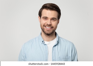 Head shot portrait smiling attractive confident millennial man wearing blue shirt posing on grey studio background, guy with bristle having white toothy smile advertise dental services or procedure