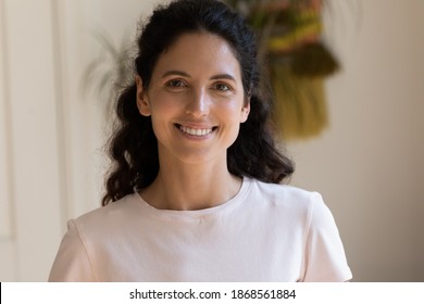 Head shot portrait smiling attractive woman looking at camera, beautiful young female with toothy smile standing at home, posing for profile picture, happy blogger recording vlog, video call