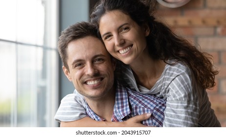 Head Shot Portrait Of Smiling Beautiful Loving Sincere Family Couple Posing Together In Own House. Affectionate Happy Beautiful Millennial Hispanic Woman Cuddling Handsome Man, Looking At Camera.