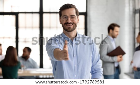 Head shot portrait smiling businessman wearing glasses extending hand for handshake at camera, friendly hr manager greeting candidate on interview, offering deal, welcoming client at meeting