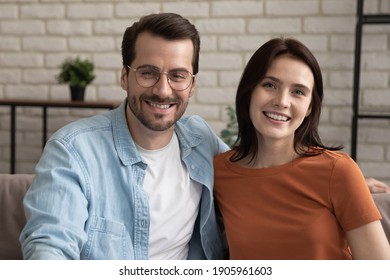 Head Shot Portrait Smiling Couple Looking At Camera, Hugging, Making Video Call To Relatives Or Friends, Sitting On Cozy Couch At Home, Happy Man Wearing Glasses And Woman Bloggers Shooting