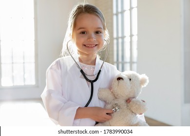 Head Shot Portrait Smiling Cute Little Girl Pretending Doctor, Pretty Preschool Child Wearing White Coat Uniform With Stethoscope Looking At Camera, Playing With Fluffy Toy Bear Patient, Healthcare